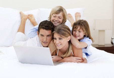 A family relaxing together on a bed while using a laptop, representing comfort and connection | MSC Cruises A family relaxing together on a bed while using a laptop, representing comfort and connection | MSC Cruises