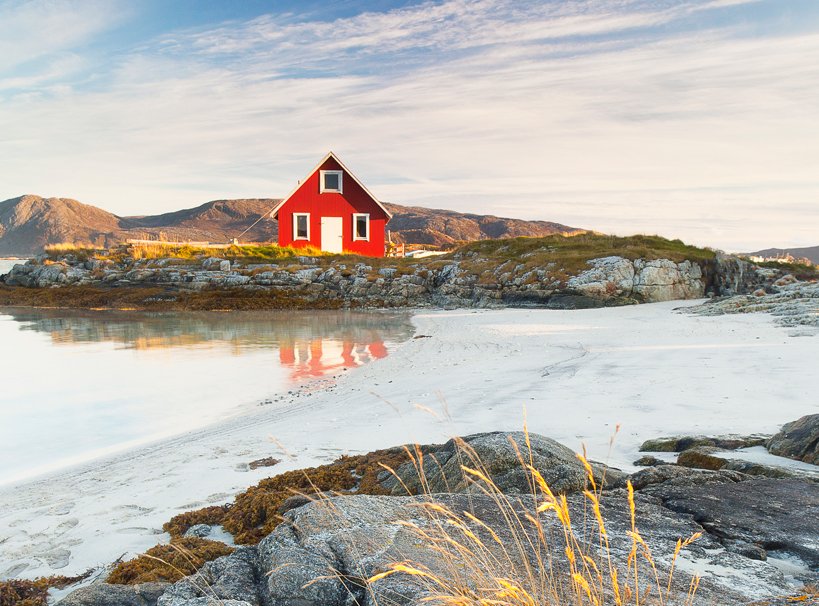 A red coastal cabin on a rocky shore with white sand and calm waters | MSC Cruises