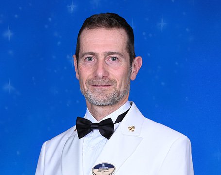 A crew member in a white uniform with a bow tie against a starry blue background | MSC Cruises