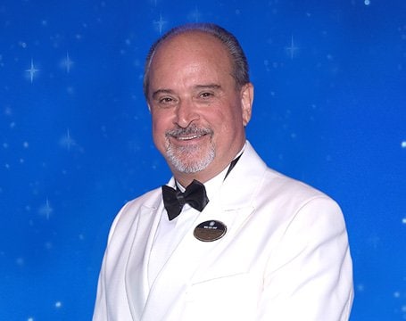 A crew member in a white uniform with an MSC Cruises badge against a starry blue background | MSC Cruises A crew member in a white uniform with an MSC Cruises badge against a starry blue background | MSC Cruises