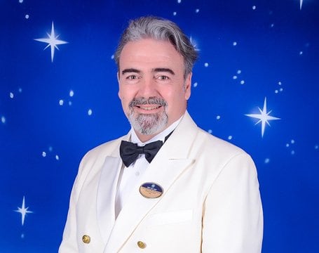 Crew member in a white formal uniform with a starry blue background | MSC Cruises Crew member in a white formal uniform with a starry blue background | MSC Cruises