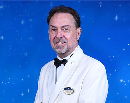 A crew member in a white uniform with a bow tie against a starry blue background | MSC Cruises A crew member in a white uniform with a bow tie against a starry blue background | MSC Cruises