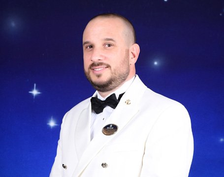A crew member in a white formal uniform against a starry background | MSC Cruises A crew member in a white formal uniform against a starry background | MSC Cruises
